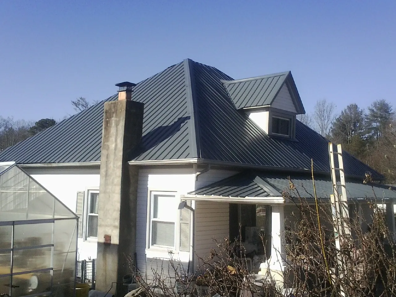 Dark blue standing seam metal roof on a white farmhouse with dormer — Slate & Tile Roof Repair by Roofing Brothers in Jackpot