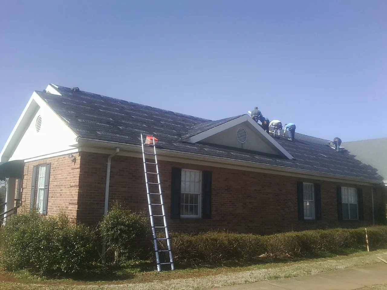 Crew tearing shingles off a brick ranch roof with a ladder set — Metal Roof Repair work by our crew in Jackpot