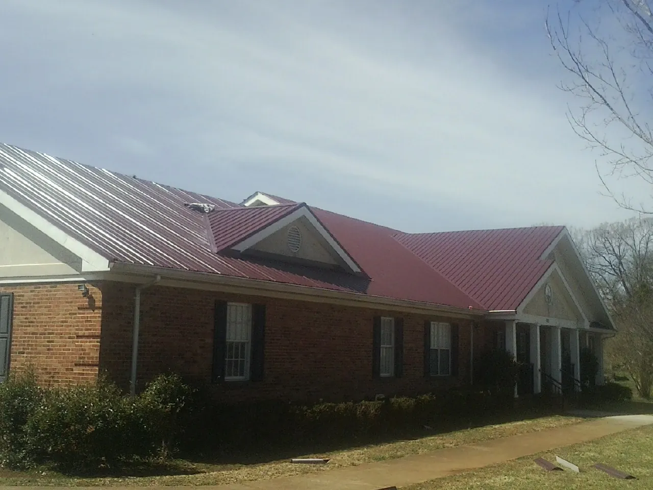 Red metal roof with gabled entries on a long brick building, from a Hail Damage Roof Repair job in Jackpot