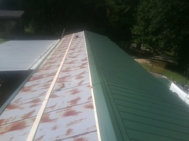 Old rusted panels beside newly installed green metal roofing — Wind Damage Roof Repair by Roofing Brothers in Jackpot