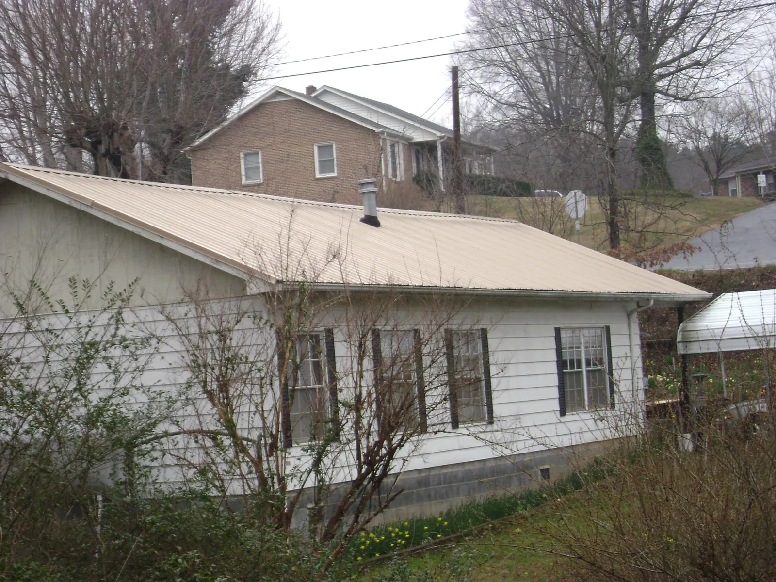 Tan metal roof on a white sided house set into a hillside — Commercial Roofing by Roofing Brothers in Jackpot